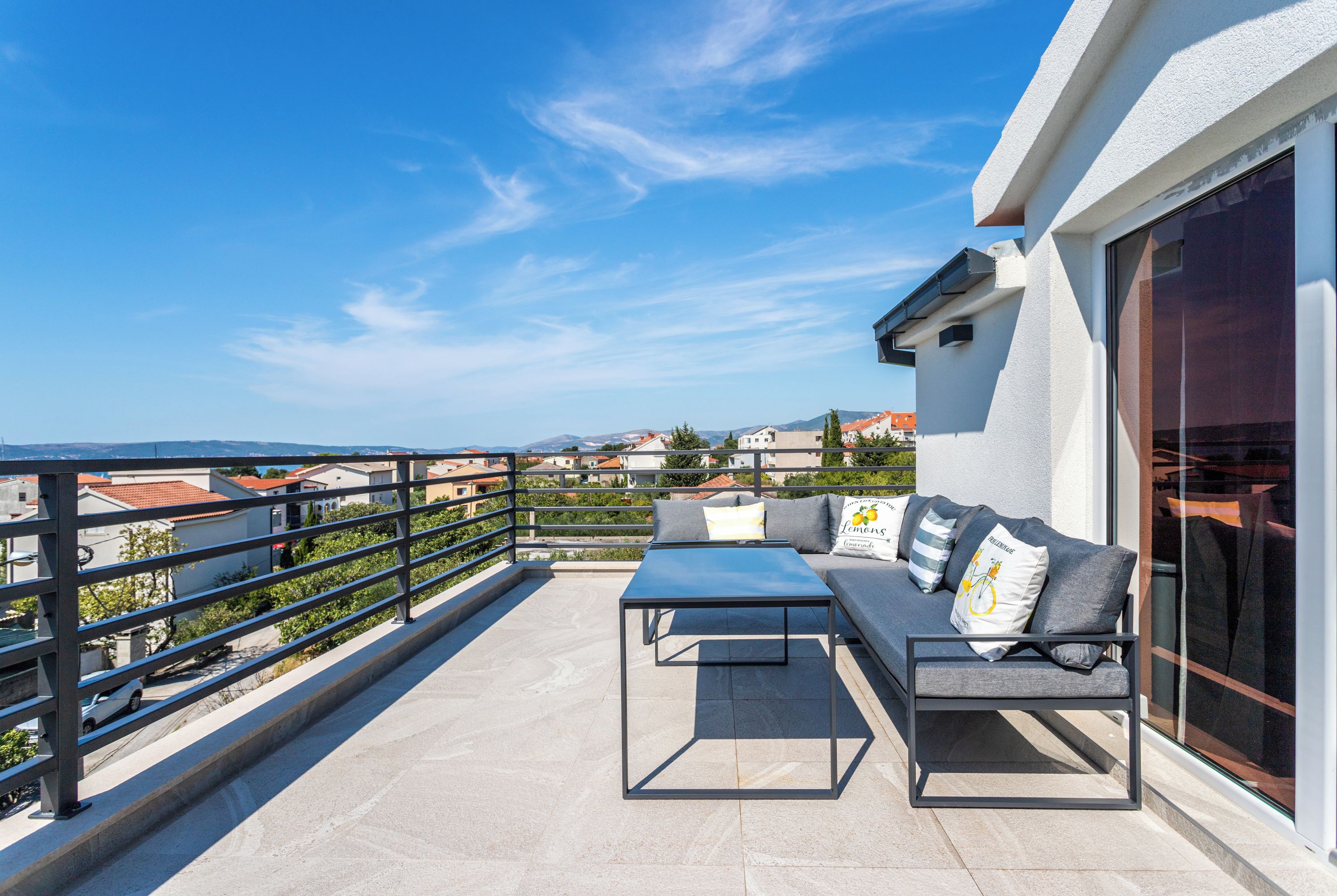 Varanda com sofá, mesa e grade, com vista para uma área residencial.