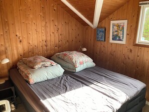 Um quarto com painéis de madeira, uma cama, uma escrivaninha e uma janela.