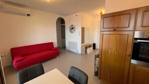 A compact living space with a red sofa, a dining table with chairs, a kitchen area with wooden cabinets, and a radiator. - Marenco apartment in Stresa with lake view (Stresa)