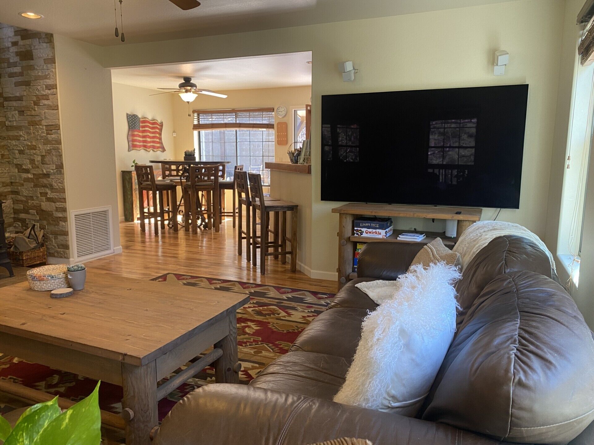 A living room with a leather couch, wooden coffee table, and a flat-screen TV. There is a dining area with a table and chairs in the background.