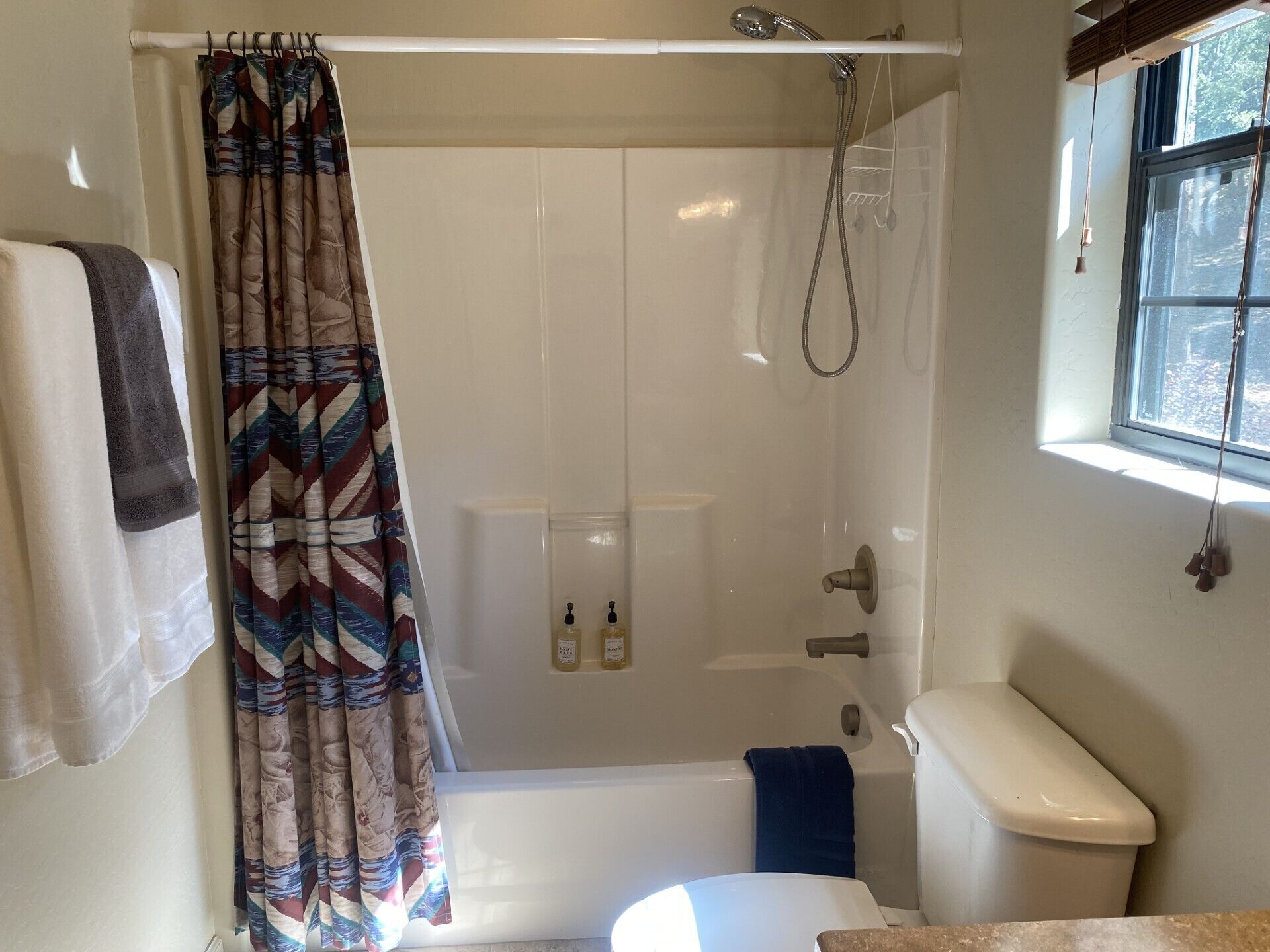 Et badeværelse med bruser, toilet og et vindue.