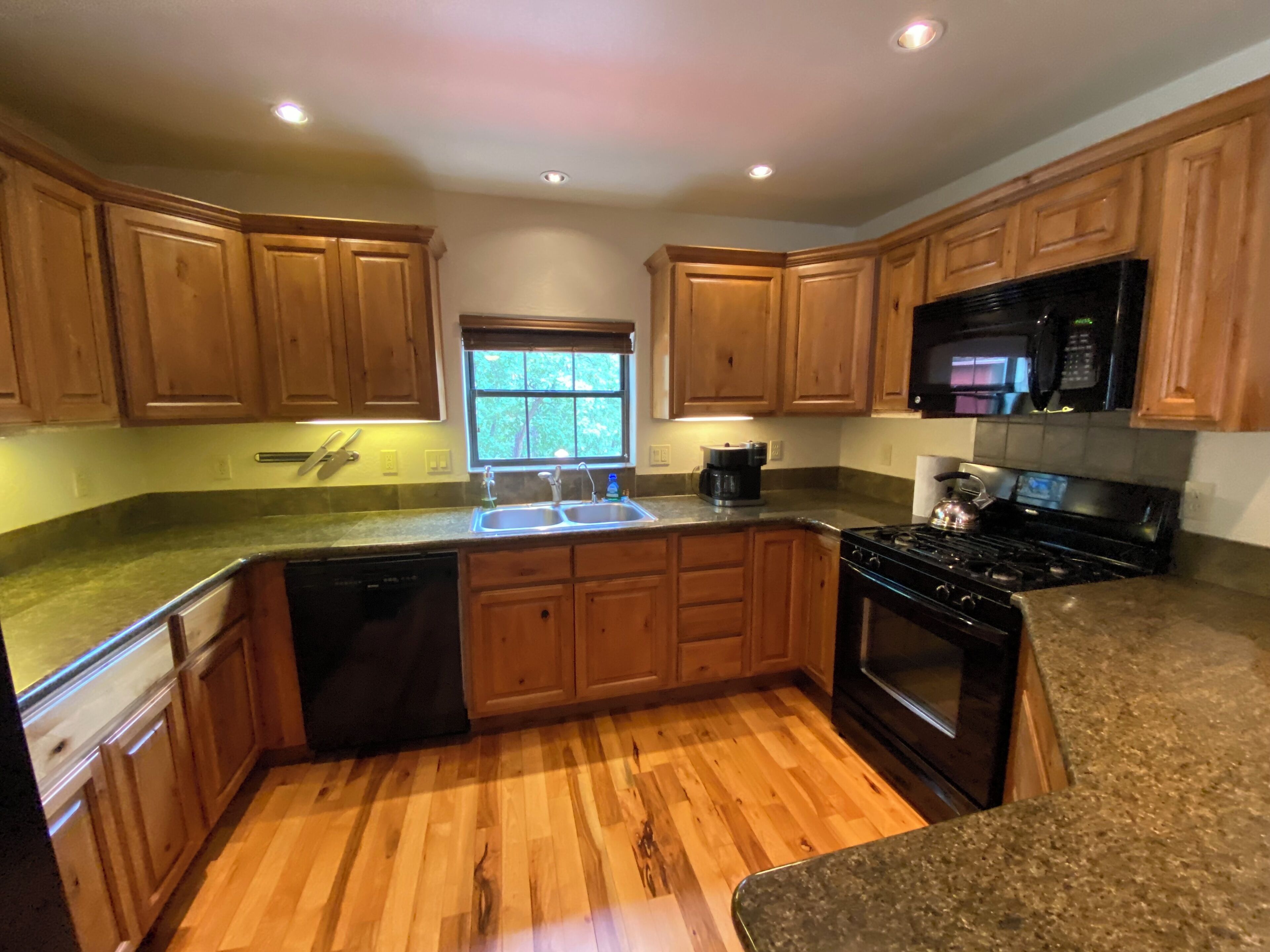 Una cocina con armarios de madera, un lavamanos de acero inoxidable, una estufa y un microondas.