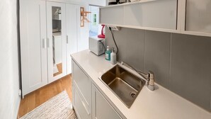 Een moderne keuken met witte kasten, een roestvrijstalen spoelbak en een aanrecht met een waterkoker en een rode apparate.'