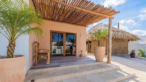 Un bâtiment doté d’un toit de chaume, d’une pergola en bois et d’un palmier.