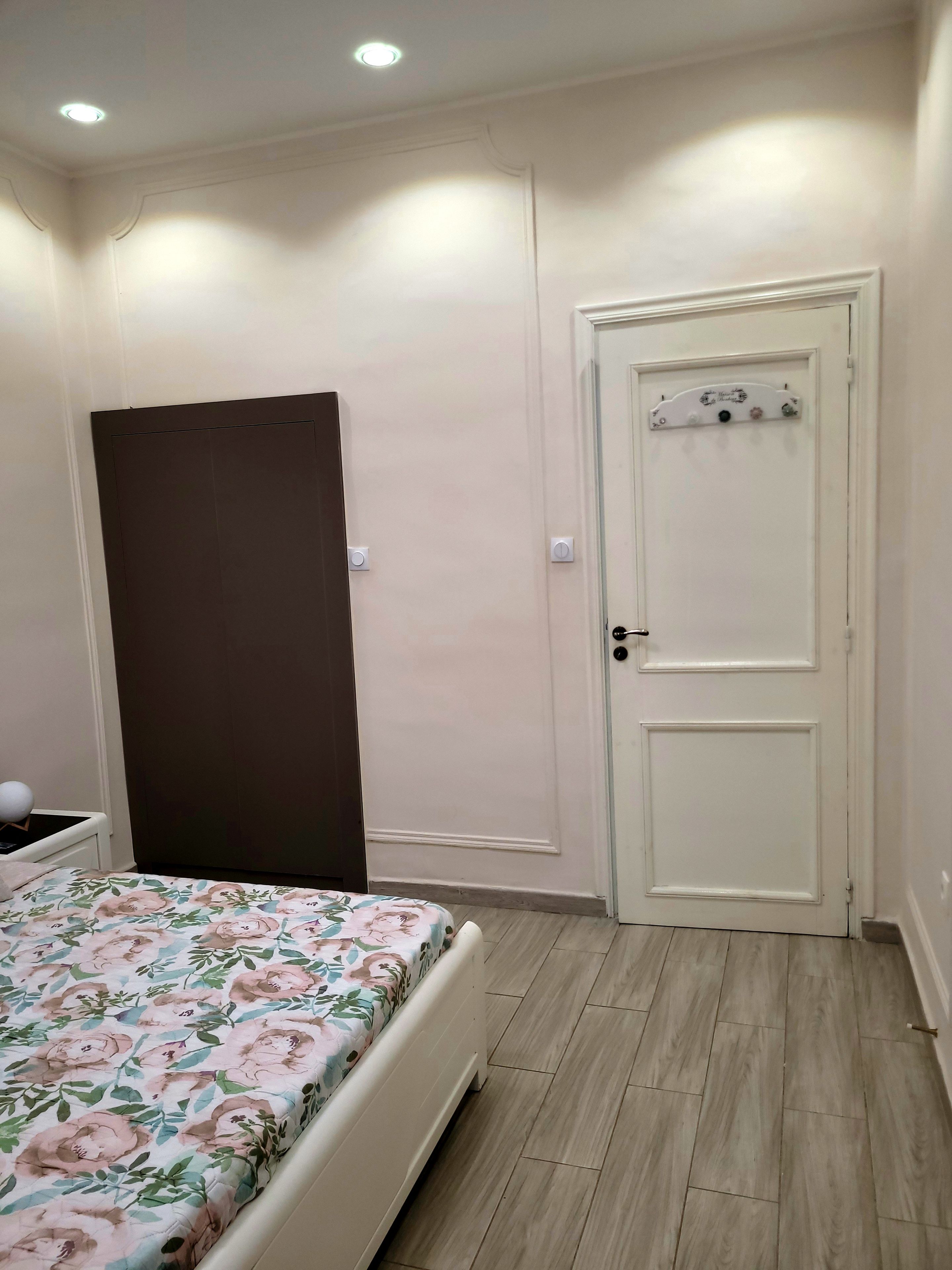 A bedroom with a bed, a wardrobe, a door, and a light switch on the wall.