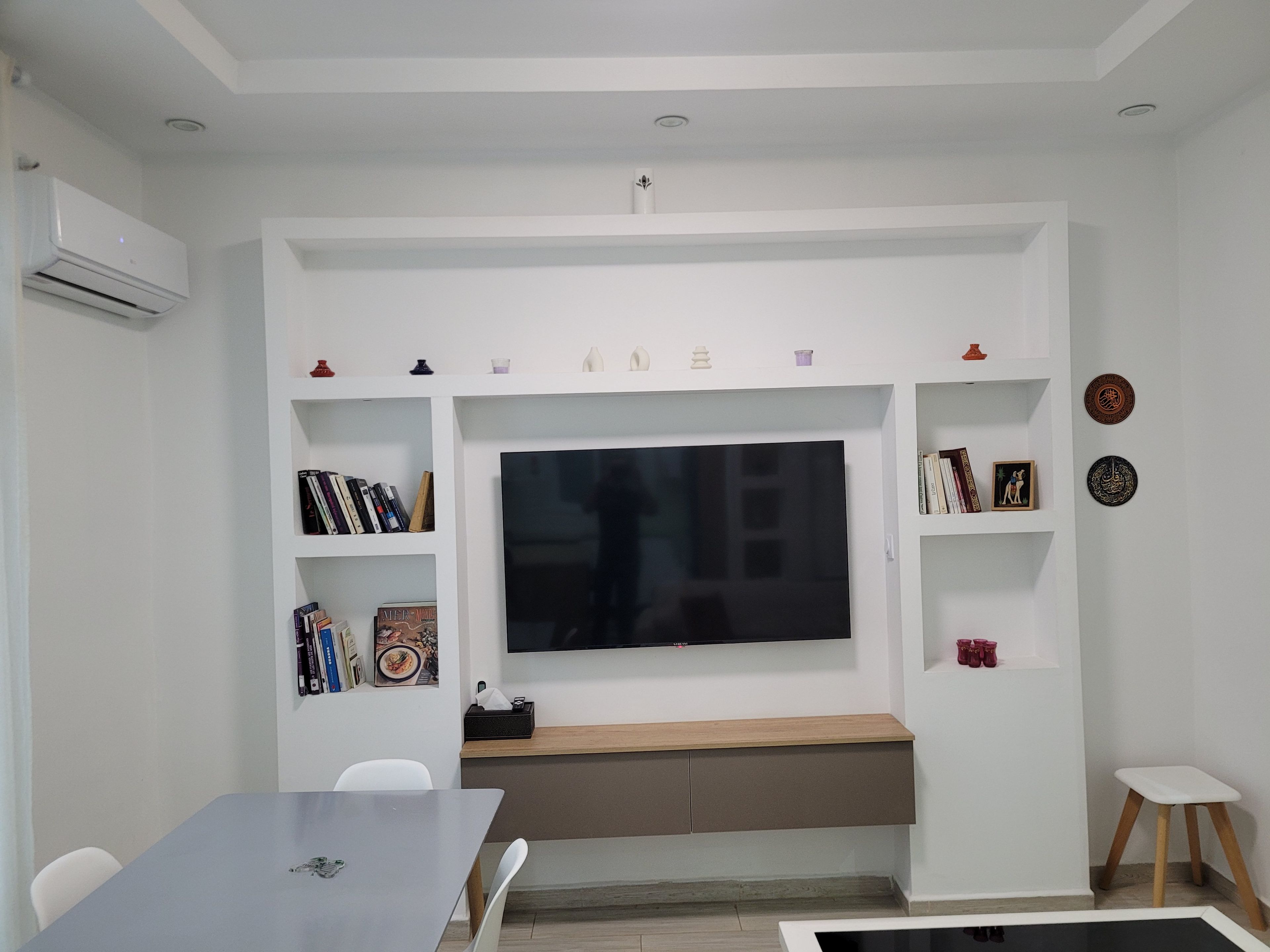A modern living room with a flat-screen TV mounted on the wall, a built-in bench, and a small table with chairs.