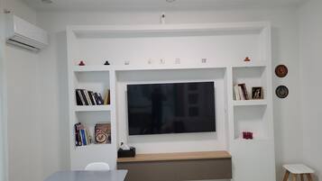 A modern living room with a flat-screen TV mounted on the wall, a built-in bench, and a small table with chairs.