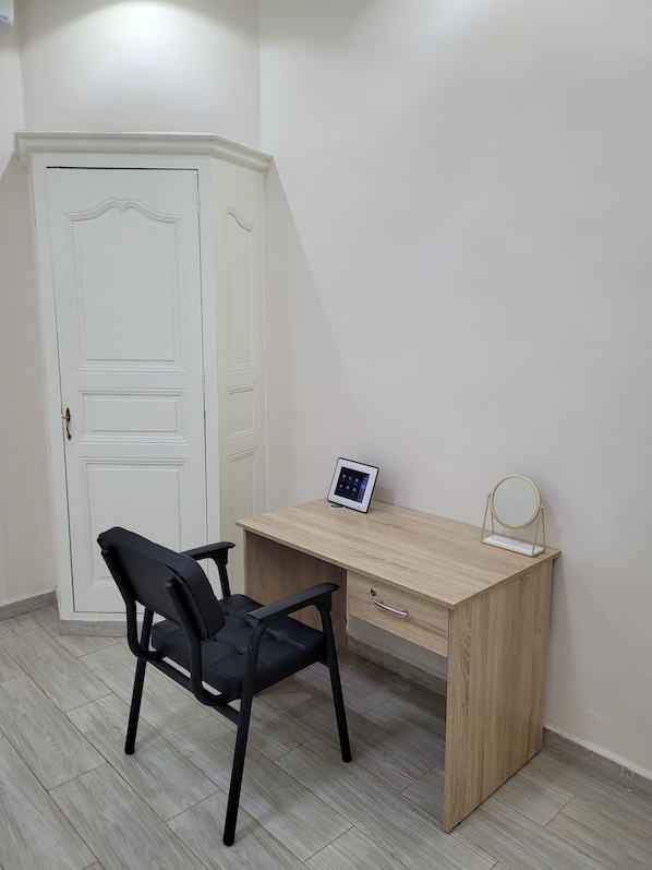 A room with a wooden desk, a black chair, a white door, and a small round mirror on the desk.