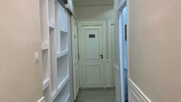 A narrow hallway with white walls, a door at the end, and a flat-screen TV mounted on the wall.