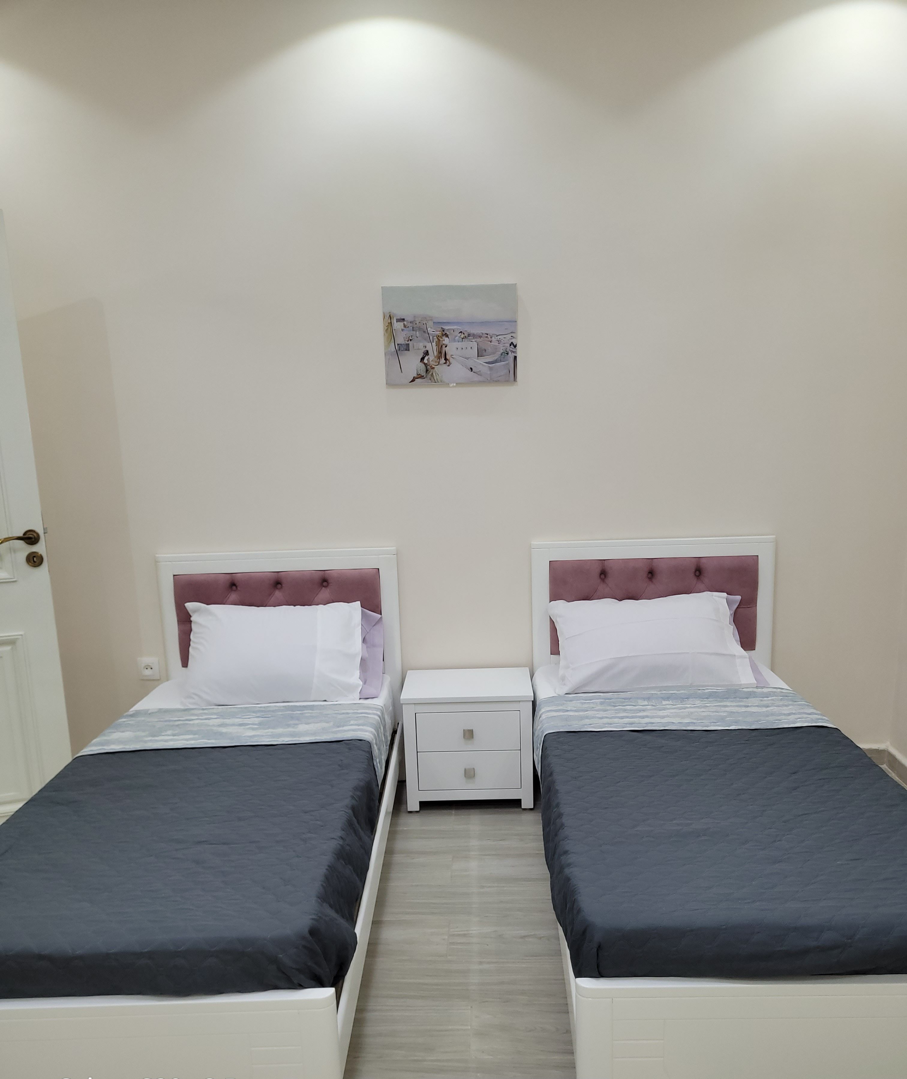 A twin room with two beds, a nightstand, a drawer, and a painting on the wall.