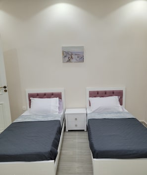 Een tweepersoonskamer met twee bedden, een nachtkastje, een lade en een schilderij aan de muur.