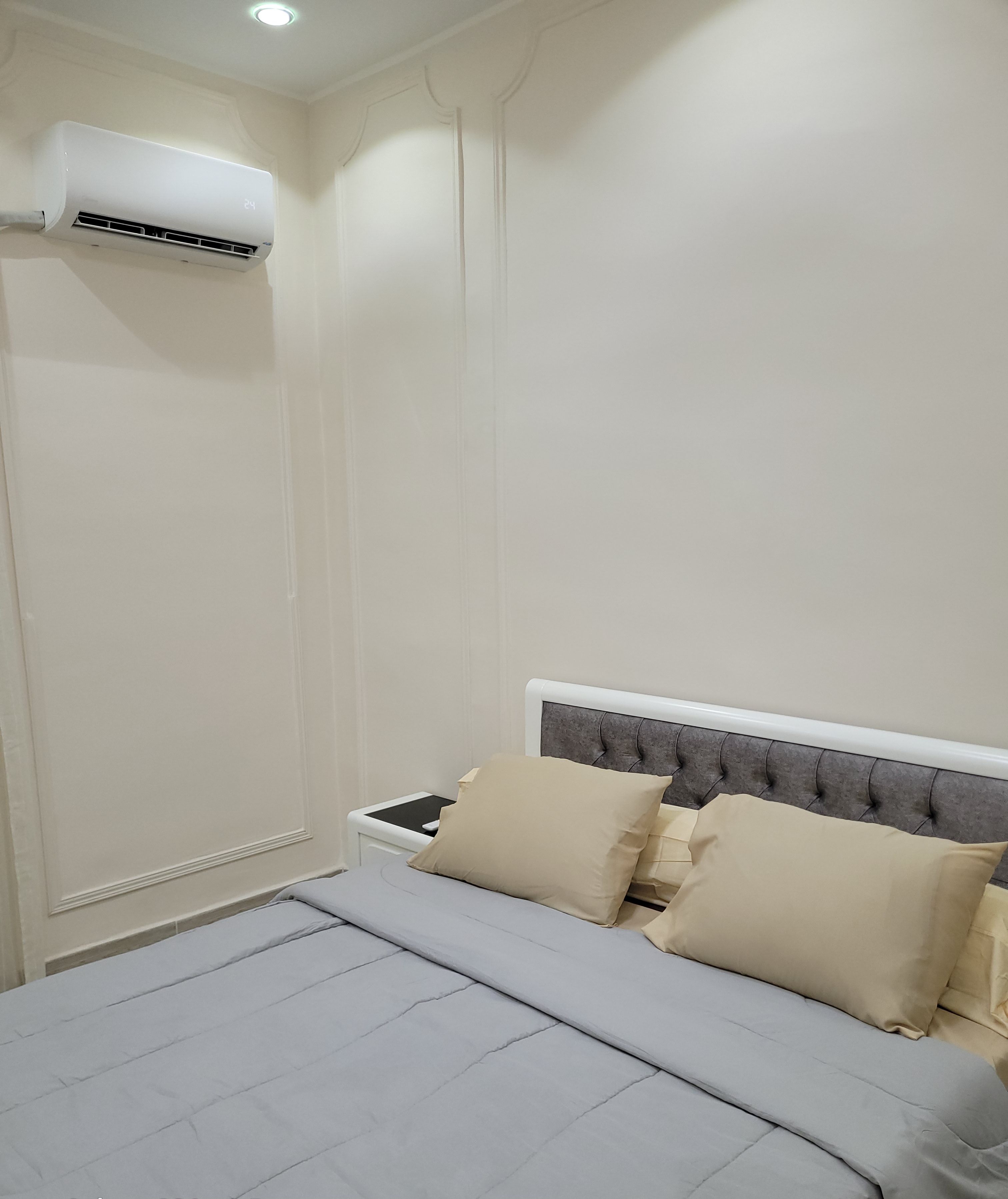 A bedroom with a bed, pillows, a bedside table, and an air conditioning unit.