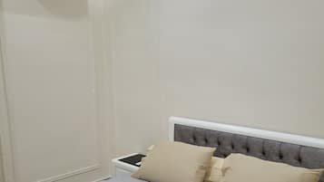 A bedroom with a bed, pillows, a bedside table, and an air conditioning unit.