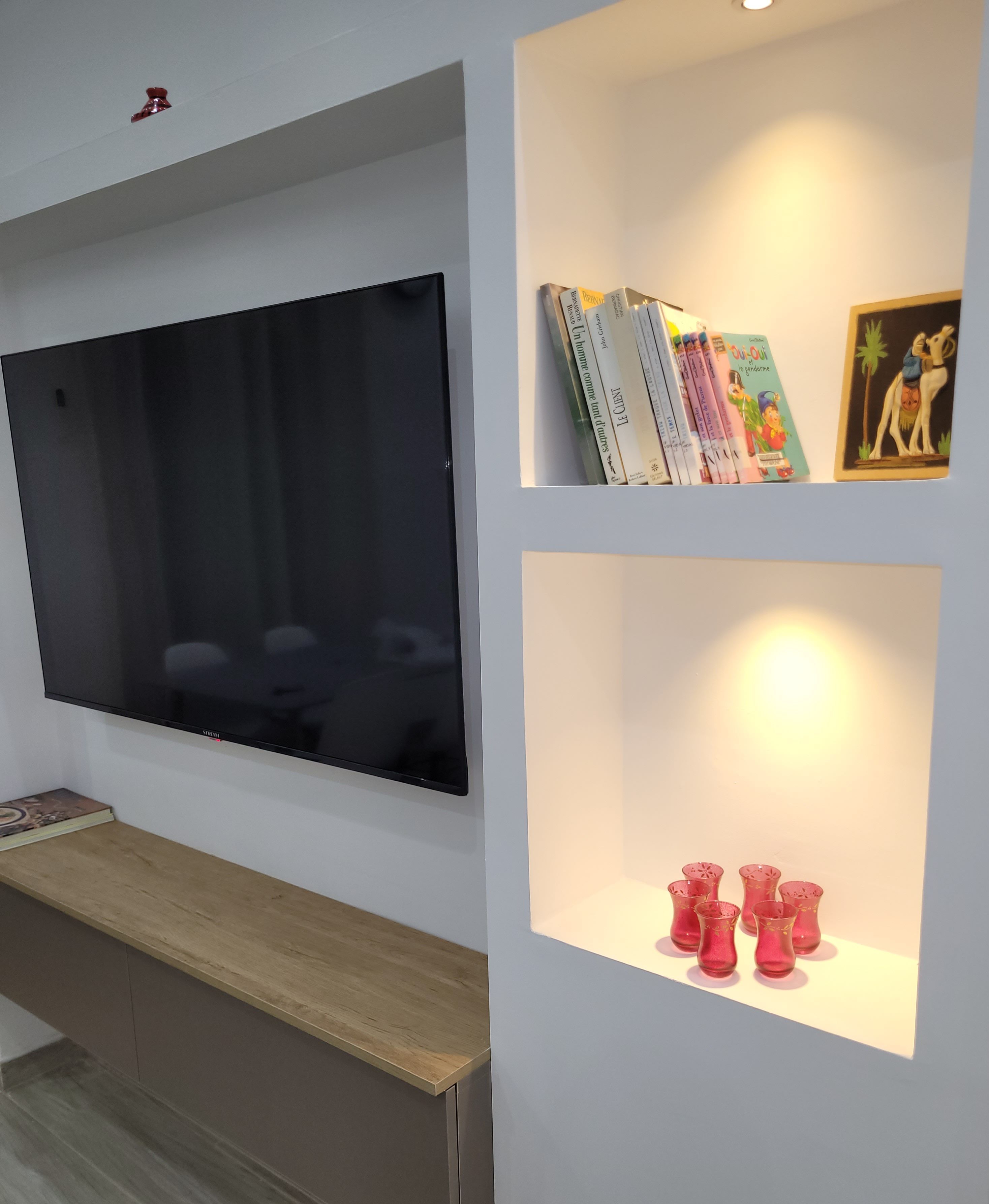 A wall-mounted TV, a shelf with books and a framed picture, and a shelf with decorative vases.