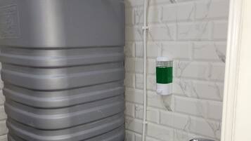 A bathroom with a large grey water tank, a green soap dispenser, and a stainless steel sink.