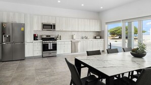A modern kitchen with white cabinetry, stainless steel appliances, and a dining area with a marble table and chairs.