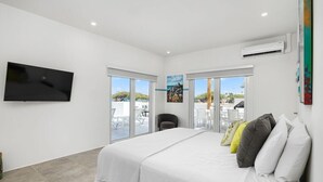 A hotel room with a bed, a flat-screen TV, a large window, and an air conditioning unit.