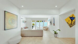 A spacious living area with a central seating area, a large abstract painting on the left, and a potted plant on the right.