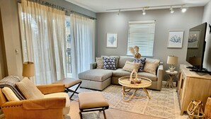 Una sala de estar con un sofá modular, una mesita redonda y un mueble para televisión.