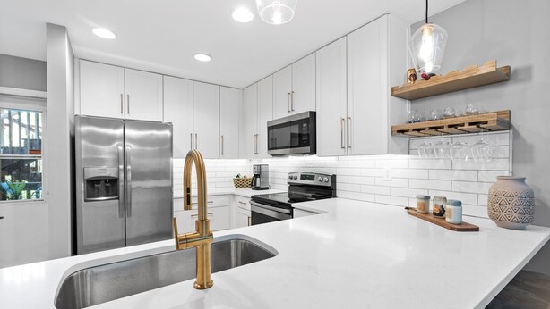 Una cocina moderna con armarios blancos, electrodomésticos de acero inoxidable y una isla grande con un grifo dorado.