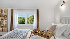 A bedroom with a large window, a bed with white linens, a wooden bedside table with breakfast items, and a wall-mounted light fixture. - Cozy home in Mirlovic Zagora (Mirlovic Zagora)