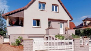 Une maison à deux étages avec un toit rouge, des murs extérieurs blancs et une clôture en bois peinte en blanc.