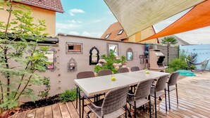 Une terrasse extérieure avec une table et des chaises, entourée de plantes et agrémentée d’une pergola.