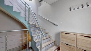 Un escalier avec une rampe en métal, une armoire en bois et un panneau mural avec des crochets.