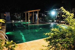 Zona de piscina nocturna amb una zona de seients coberta i una escala de piscina.