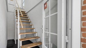 Una escalera con peldaños de madera que lleva a una puerta con paneles de vidrio satinado y un letrero rojo con una 'N' blanca.