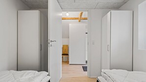 Habitación de hotel con dos camas, una viga de techo de madera y vista hacia otra habitación con una silla y una mesa.