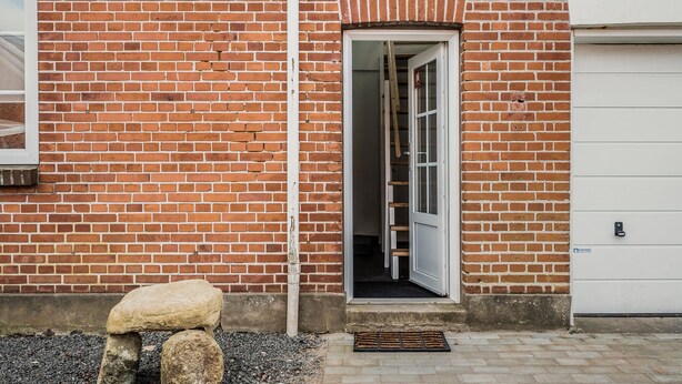 Un edificio de ladrillo con una puerta de garaje blanca, un banco de piedra y un estrecho acceso al interior.