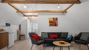 Una sala de estar moderna con un sofá gris, dos sillones, una mesita redonda y una cocina con microondas y refrigerador.