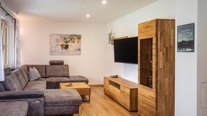 A modern living room with a sectional sofa, a wooden cabinet, and a flat-screen TV mounted on the wall. - Pet friendly apartment (Rußbach am Pass Gschütt)