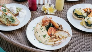 A table set with various plates of food, including eggs benedict and a croissant, along with two drinks and a napkin set. - Embrace Ancient Bali at Umah Bali Kuno Villas (Gianyar)