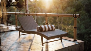 A wicker lounge chair with a striped towel on a tiled patio with a bamboo railing. - Embrace Ancient Bali at Umah Bali Kuno Villas (Gianyar)
