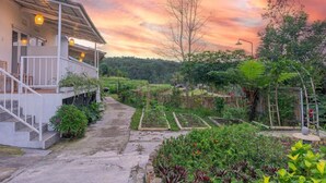 A two-story building with a covered porch and a garden with various plants and a pathway. - Santya Loka Lodge and Twin Waterfall (Tabanan)