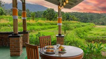 An outdoor dining area with a brick table and chairs, surrounded by lush greenery and a view of terraced fields.
