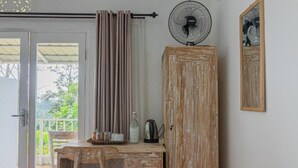 A rustic wooden desk with a chair, a small table with a bottle and a kettle, a wooden cabinet, and a standing fan. - Santya Loka Lodge and Twin Waterfall (Tabanan)