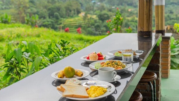A table with breakfast items including toast, eggs, and fruit, set against a lush green landscape. - Santya Loka Lodge and Twin Waterfall (Tabanan)