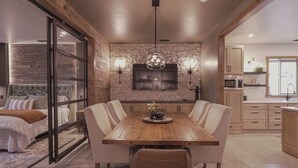 Un comedor moderno con una mesa y sillas de madera, una pared de piedra y una cocina al fondo.