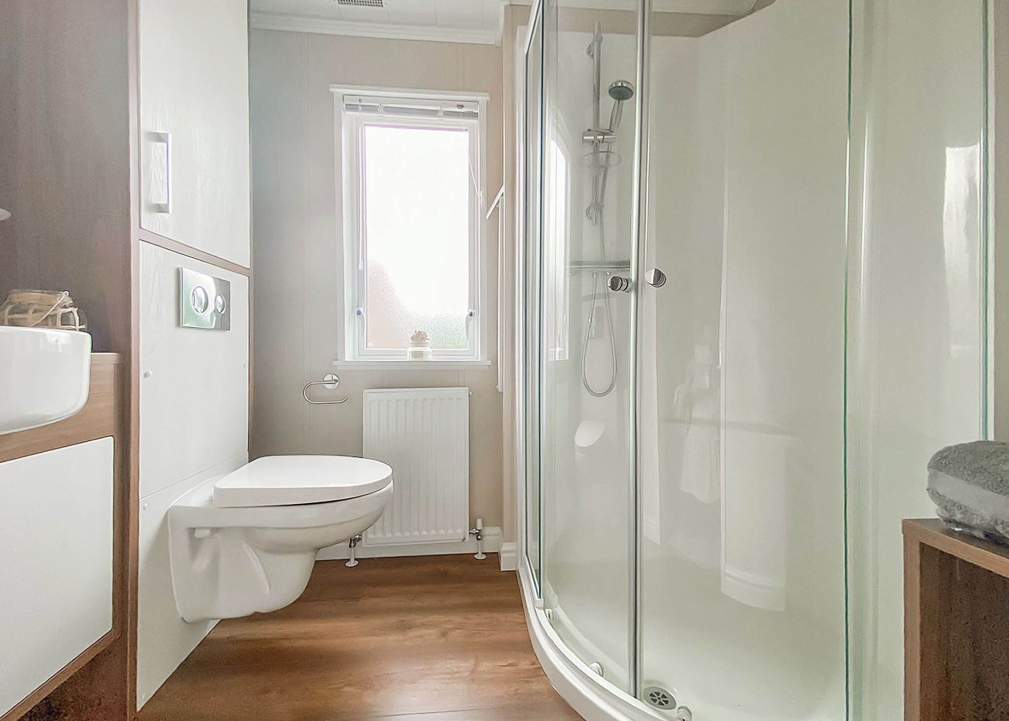 A modern bathroom with a glass shower enclosure, a toilet, and a window.