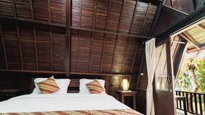A bedroom with a large bed, wooden ceiling beams, a nightstand with a lamp, and a view of greenery through a balcony door. - Sandat Bali Villa (Canggu)