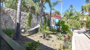 Un jardin avec différentes sortes de plantes, un hamac et un mur de pierre.