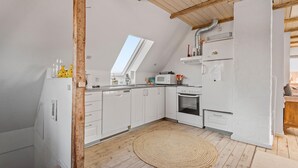 A compact kitchen with white cabinets, a microwave, a stove, and a refrigerator. There's a wooden beam ceiling and a window providing natural light. - Beautiful apartment in Ribe with WiFi (Ribe)