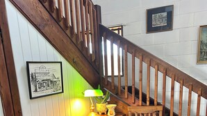 Een houten bureau met een lamp en een stoel, een trap met houten leuningen, en een lijst met een foto aan de muur.