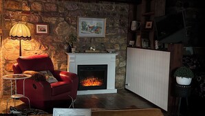 Een gezellige woonkamer met een open haard, een rode fauteuil, een bruine bank en een tafel met een kom en een ingelijst certificaat.