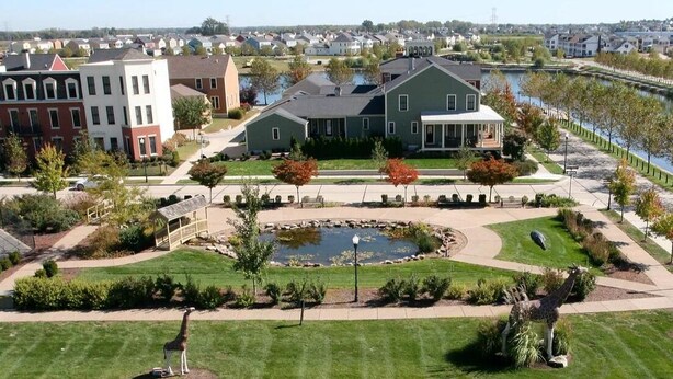 A residential area with a large house featuring a covered porch, a small pond, and a giraffe statue. - Cozy Front Lake Home in Newtown St. Charles (Saint Charles)