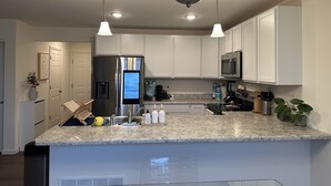 A modern kitchen with white cabinets, a stainless steel refrigerator, a microwave, and a granite countertop. - Cozy Front Lake Home in Newtown St. Charles (Saint Charles)
