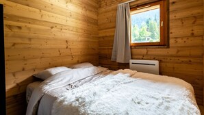 Een houten kamer met een bed, een raam met gordijn en een radiator.